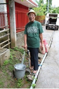 Lola Doring proudly stands by the faucet that derives water from the water system that she and fellow women-volunteers built.