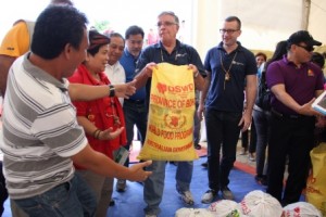 Australian Ambassador Twedell tries to carry a sack of food pack at the DSWD warehouse in Tubigon where 100 volunteers helped repack goods, while Secretary Soliman looks on.