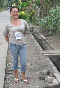 Mercy, beaming with pride, stands beside the concrete canal project that she and her fellow volunteers actively implemented.
