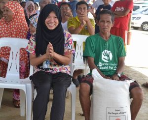 An internally displaced person happily waits for her turn to receive a sack of rice during the ceremonial turnover of rice donations from the Government of Japan.