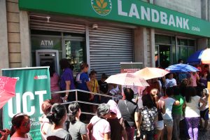 DSWD Pantawid Pamilyang Pilipino Program (4Ps) beneficiaries queue to use an automated teller machine (ATM) outside a Land Bank of the Philippines (LBP) branch after their Unconditional Cash Transfer (UCT) grants had been credited to their cash card accounts. 