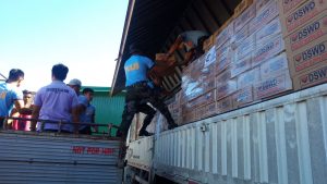 Volunteers assist in transferring boxes of family food packs (FFPs) to smaller trucks for delivery to families in disaster-affected areas.