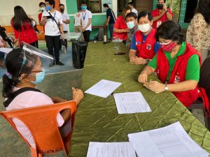 Department of Social Welfare and Development Secretary Rolando Joselito D. Bautista (in blue shirt) joins DSWD Field Office I Regional Director Marie Angela S. Gopalan (in green shirt) and Bacnotan Mayor Francisco Angelito Fontanilla (partly hidden) in handing out emergency shelter assistance to typhoon-affected families in Bacnotan, La Union.