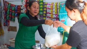 A member of the Pooc Entrepreneur Association hands out a bag of rice to a satisfied customer of their sari-sari store.